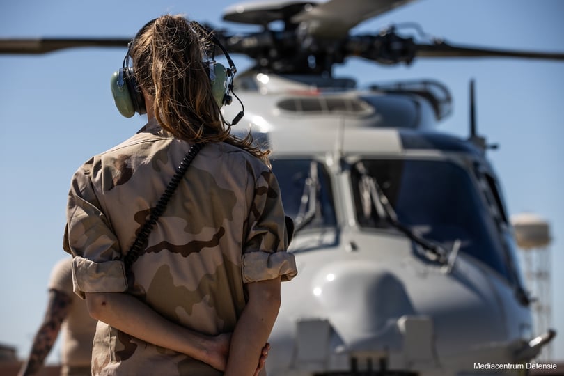 A Dutch Defence crew member seen from behind, facing a helicopter on the ground