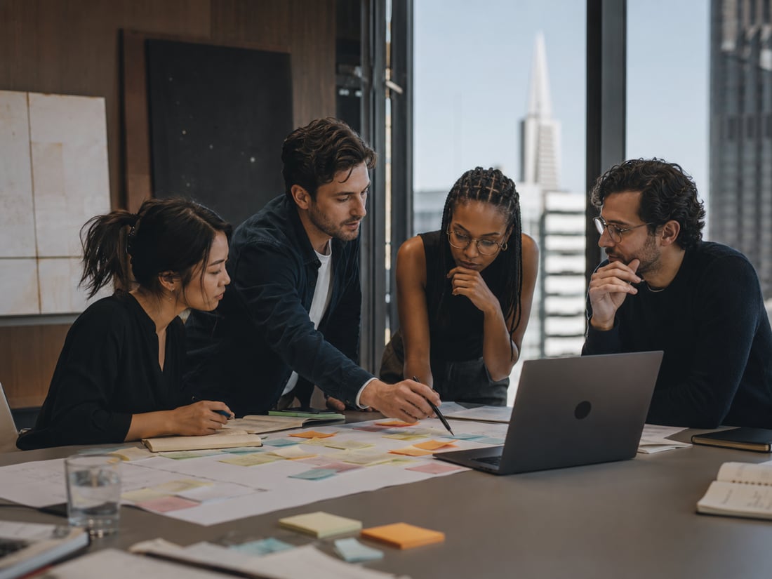 Vier collega's werken samen aan een ontwerp, aan een tafel vol notities