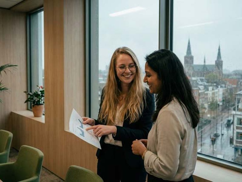Twee collega's bekijken samen een document bij een raam
